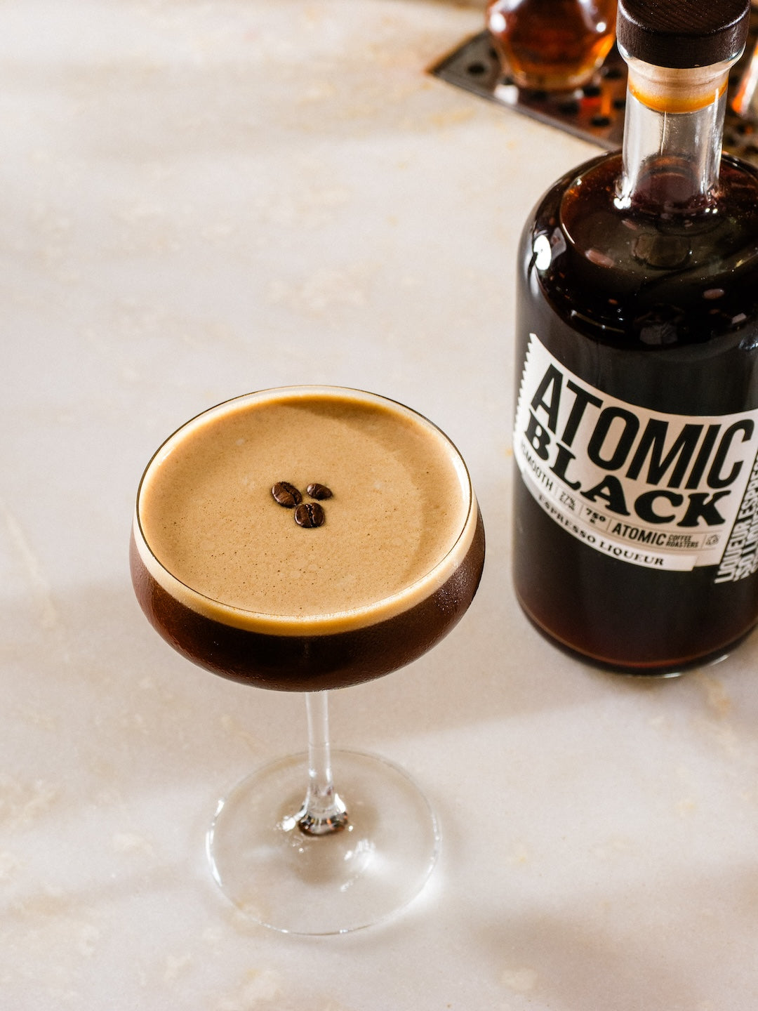 Cocktail in a glass with a bottle of 'Atomic Black' on a marble surface